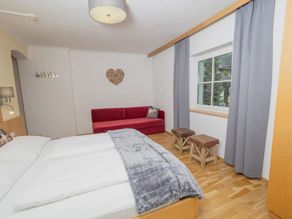 Schlafzimmer mit rotem Sofa, Fenster und Holzfußboden
