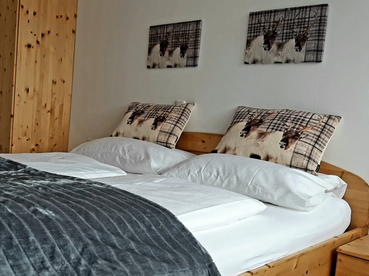 Holzbett mit graudem Bettüberwurf und Kissen, Holzschrank und Bildern an der Wand